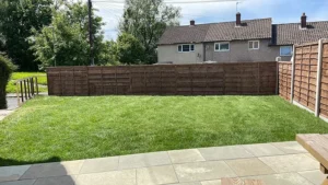 Freshly laid lawn with a stone-paved patio and wooden fencing by Drivers Building & Roofing.