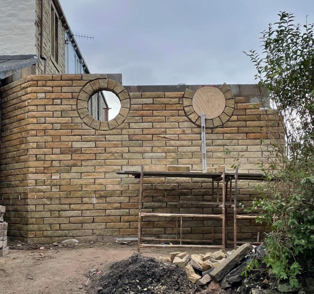 Stone masonry wall under construction with two circular window openings by Drivers Building & Roofing.