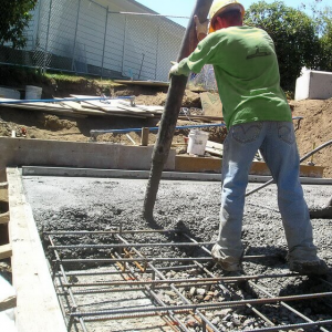 A worker pouring concrete into foundation rebar structures for solid foundations by Drivers Building & Roofing.