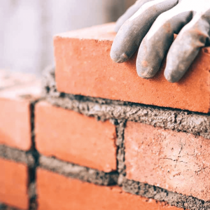one of our bricklayer carefully positioning red bricks while constructing a wall.