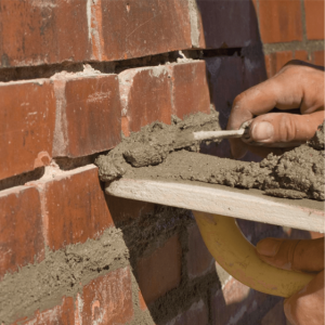 A worker applying mortar between bricks for precise pointing work by Drivers Building & Roofing.